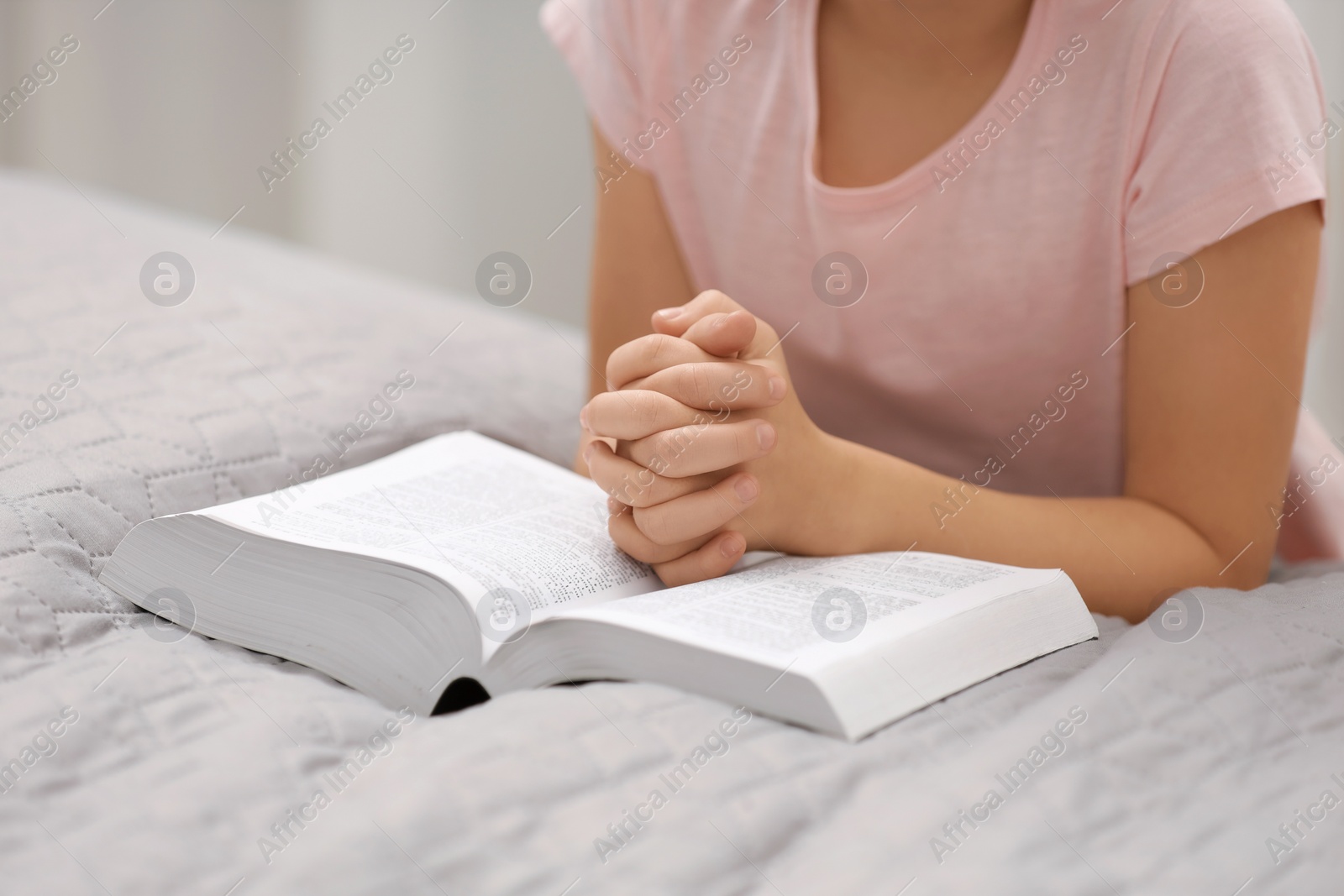 Photo of Girl holding hands clasped while praying over Bible indoors, closeup