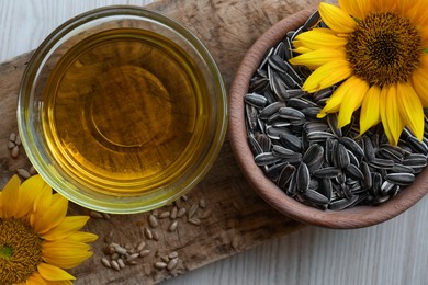 Photo of Bowl of sunflower oil and seeds on light wooden table, flat lay