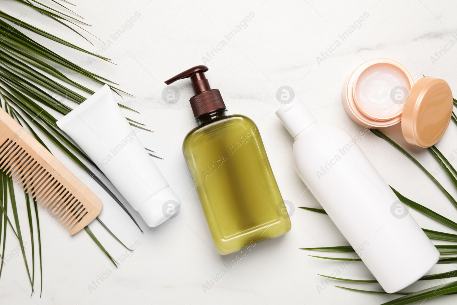 Photo of Shampoo bottles, wooden comb, hair and face mask and palm leaves on white marble table, flat lay