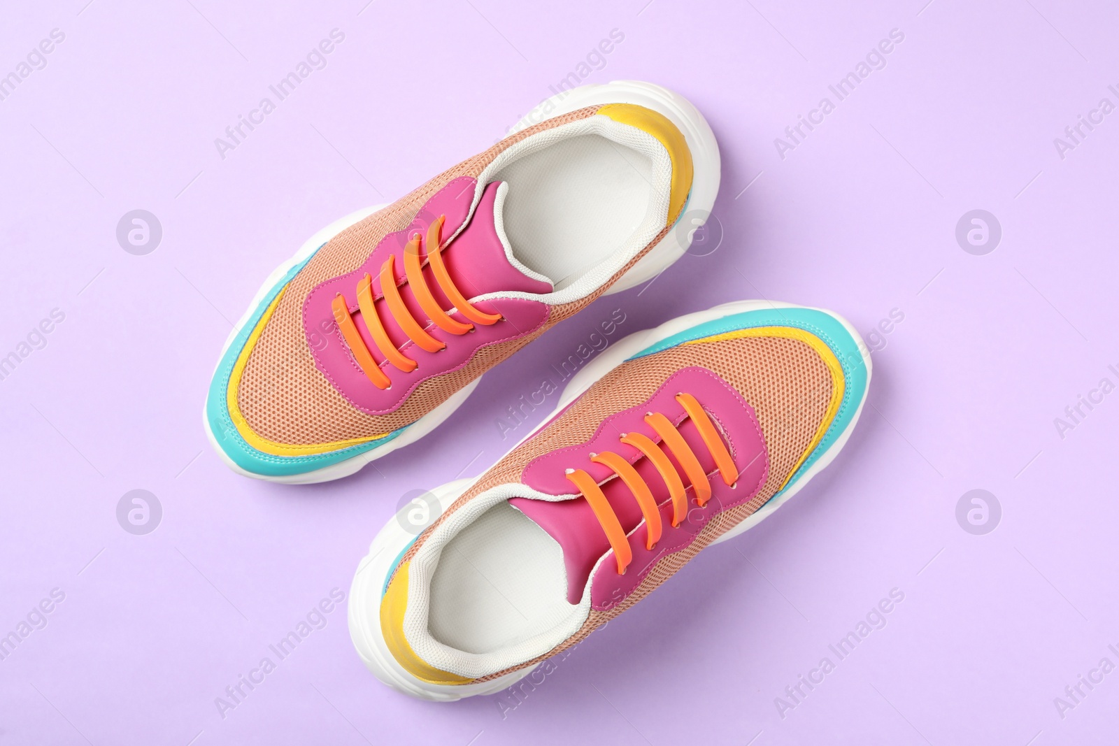 Photo of Stylish sneakers with orange silicone shoe laces on violet background, flat lay