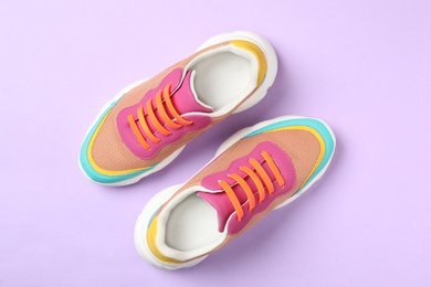 Stylish sneakers with orange silicone shoe laces on violet background, flat lay