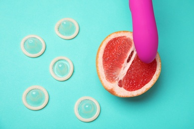 Photo of Half of grapefruit, purple vibrator and condoms on turquoise background, top view. Sex concept