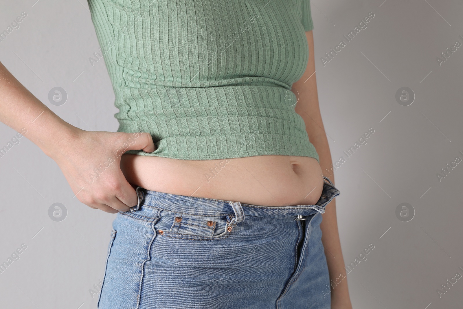 Photo of Woman wearing tight clothes on light grey background, closeup. Overweight problem