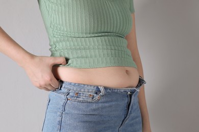 Woman wearing tight clothes on light grey background, closeup. Overweight problem