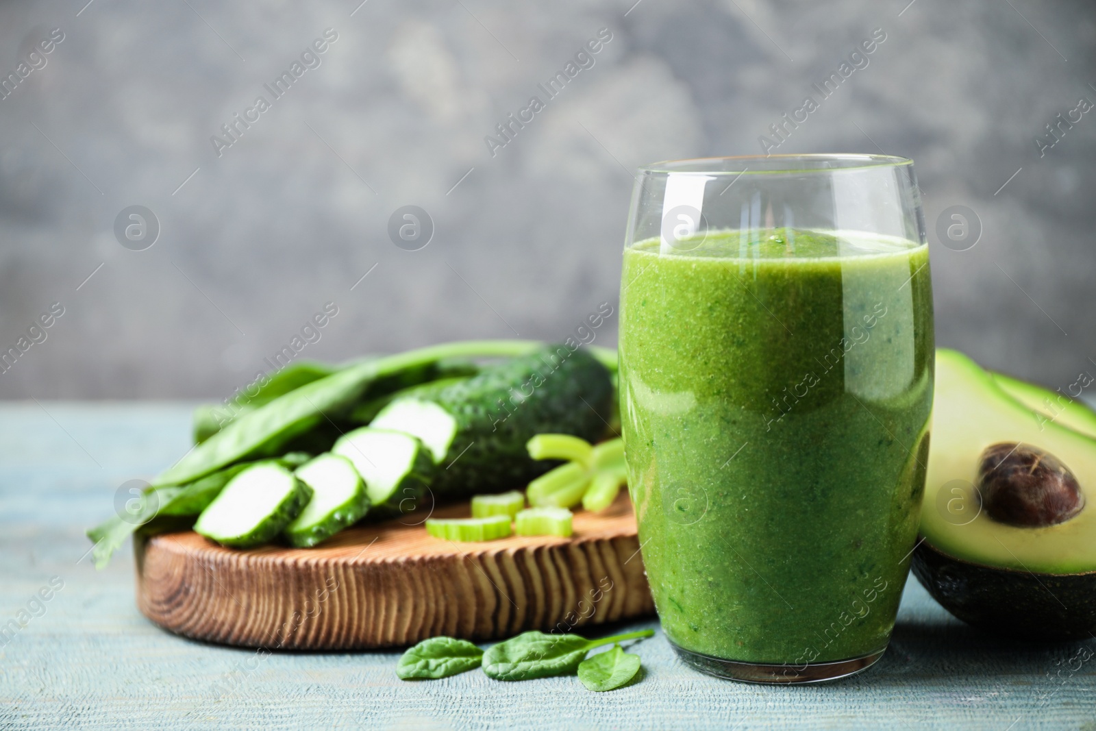 Photo of Delicious green juice and fresh ingredients on light blue wooden table. Space for text