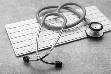 Photo of Computer keyboard with stethoscope on grey table, closeup