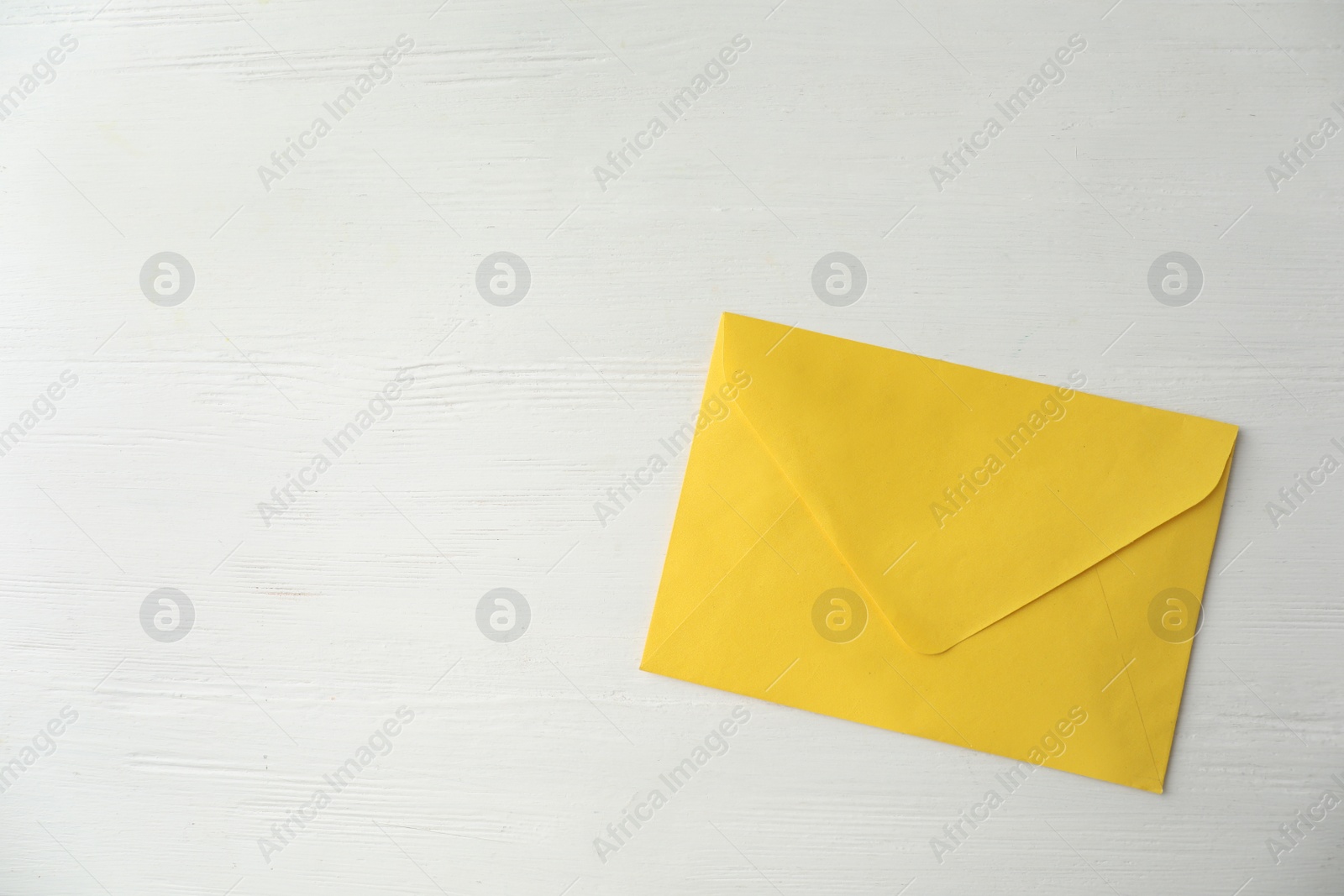 Photo of Yellow paper envelope on white wooden table, top view. Space for text