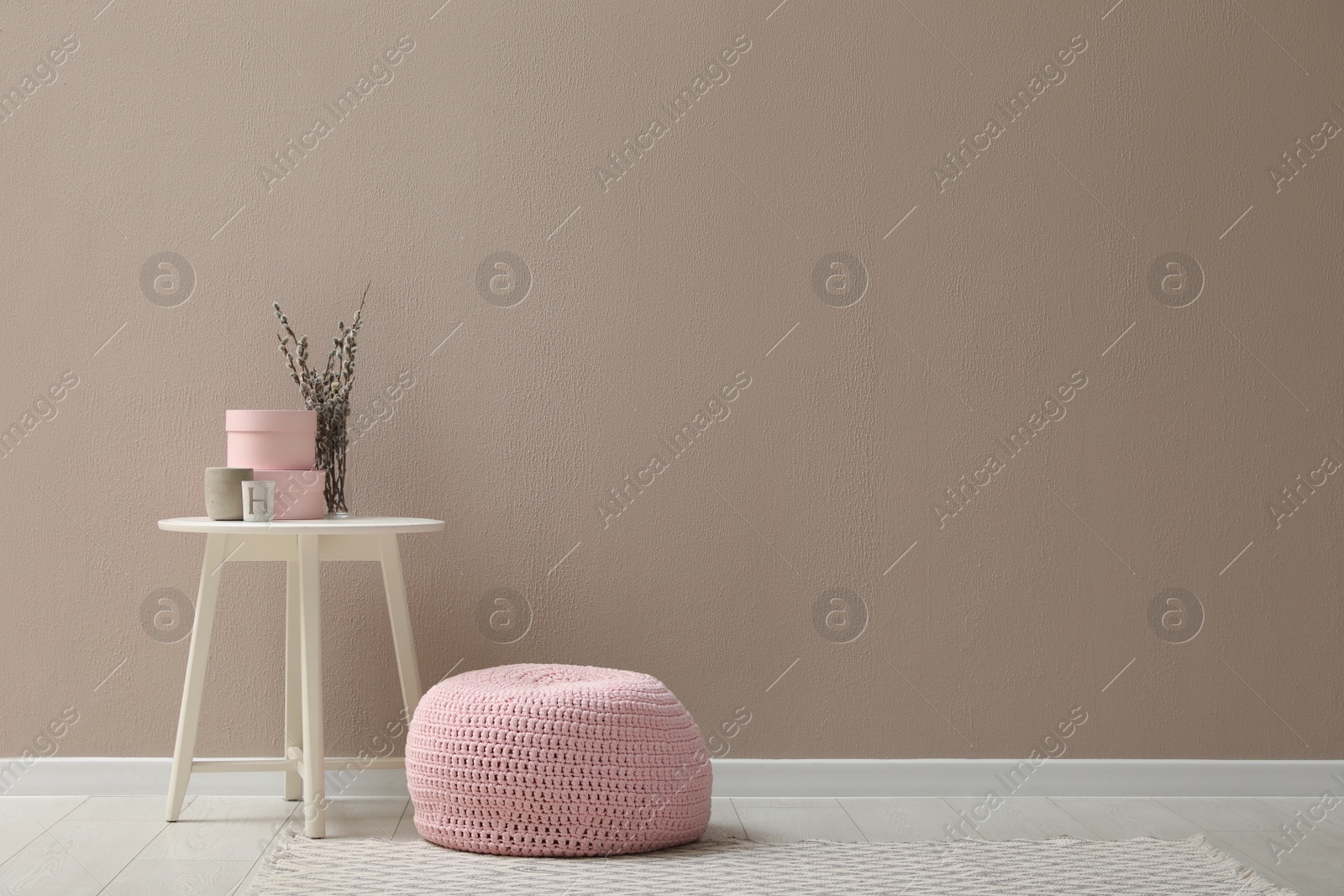 Photo of Knitted pouf and decor elements near beige wall indoors. Space for text