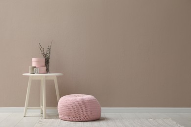 Knitted pouf and decor elements near beige wall indoors. Space for text