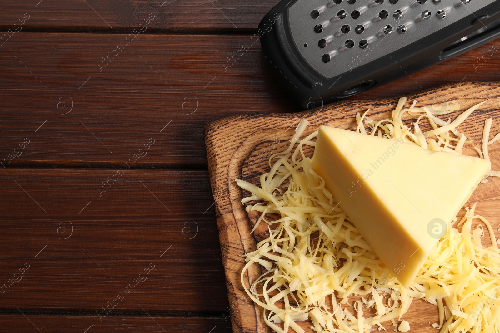 Photo of Grated, whole piece of cheese and grater on wooden table, top view. Space for text