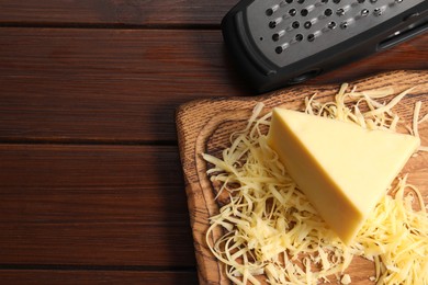 Photo of Grated, whole piece of cheese and grater on wooden table, top view. Space for text