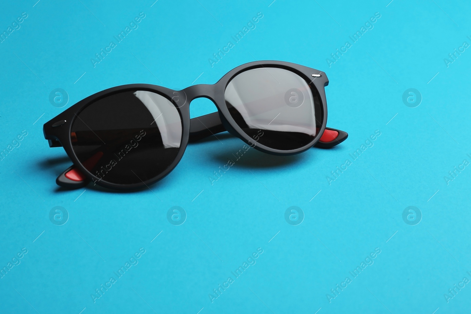 Photo of Stylish sunglasses on blue background. Fashionable accessory