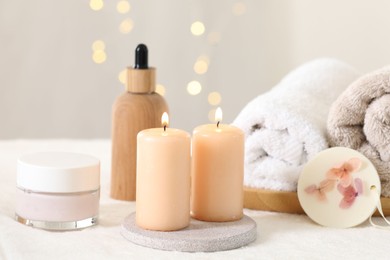 Photo of Spa composition. Burning candles and personal care products on soft white surface