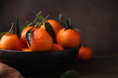 Photo of Fresh ripe tangerines with green leaves in bowl on table, closeup. Space for text