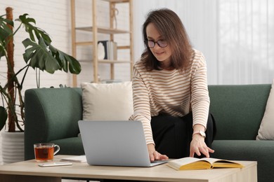 Photo of Woman with modern laptop and book learning in living room
