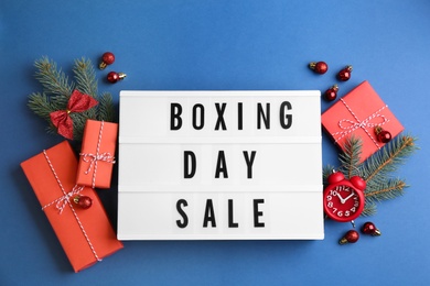 Photo of Lightbox with phrase BOXING DAY SALE and Christmas decorations on blue background, flat lay