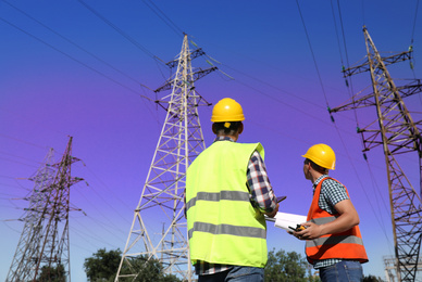 Professional electricians in uniforms near high voltage towers