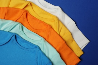 Photo of Closeup of cute baby onesies on color background, top view