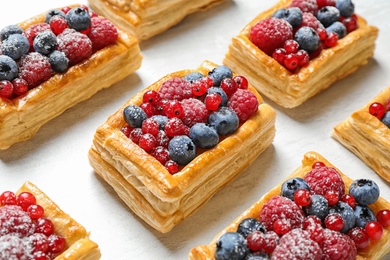 Fresh delicious puff pastry with sweet berries on light table, closeup