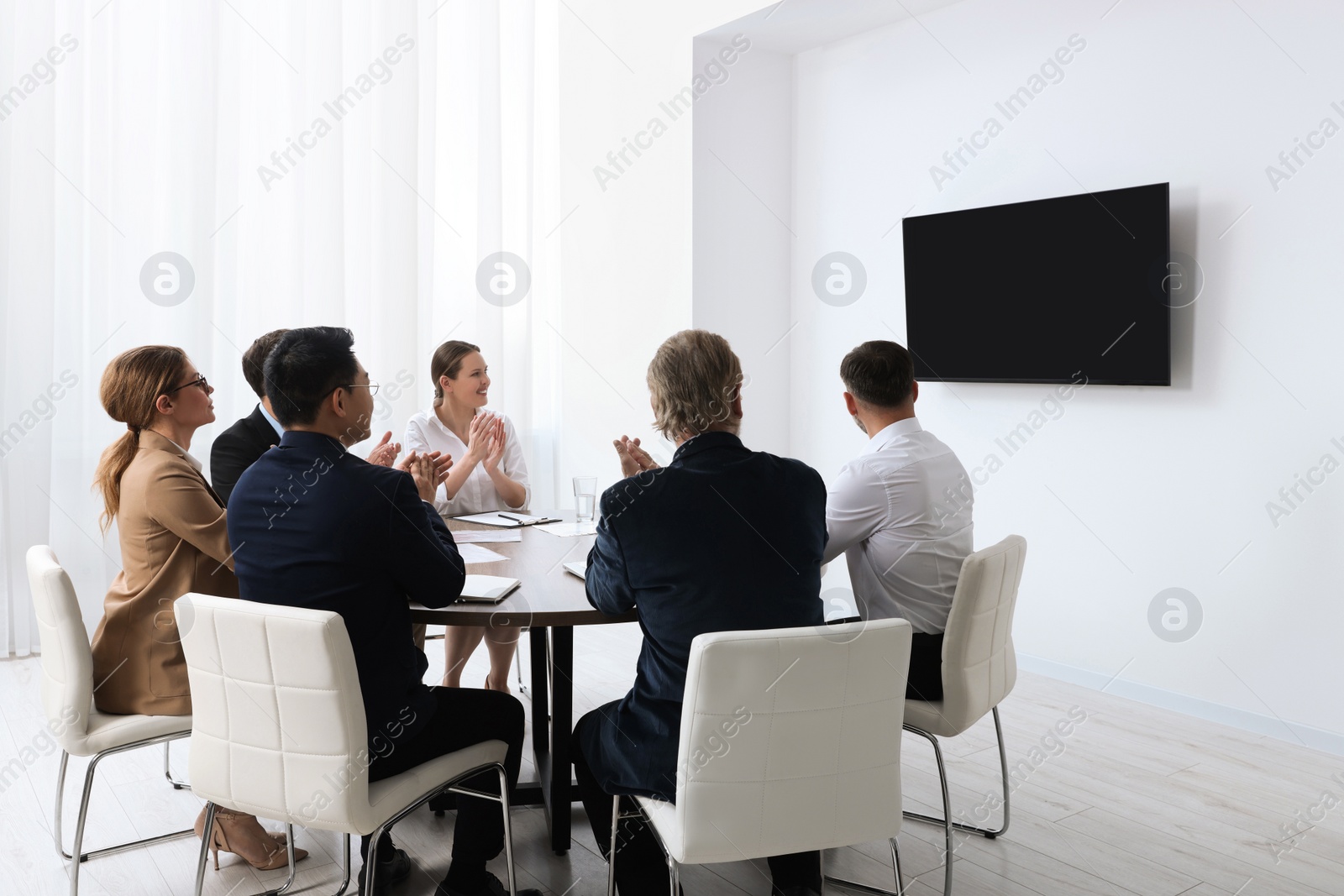 Photo of Business conference. Group of people watching presentation on tv screen in meeting room