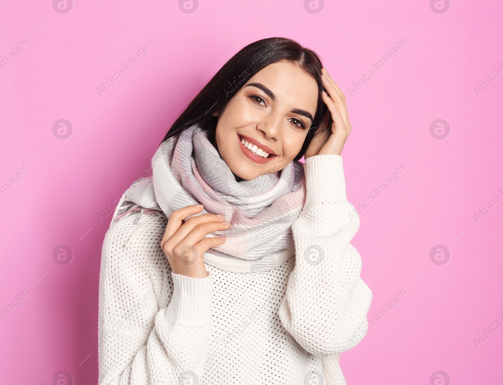 Photo of Young woman wearing warm sweater and scarf on pink background. Winter season