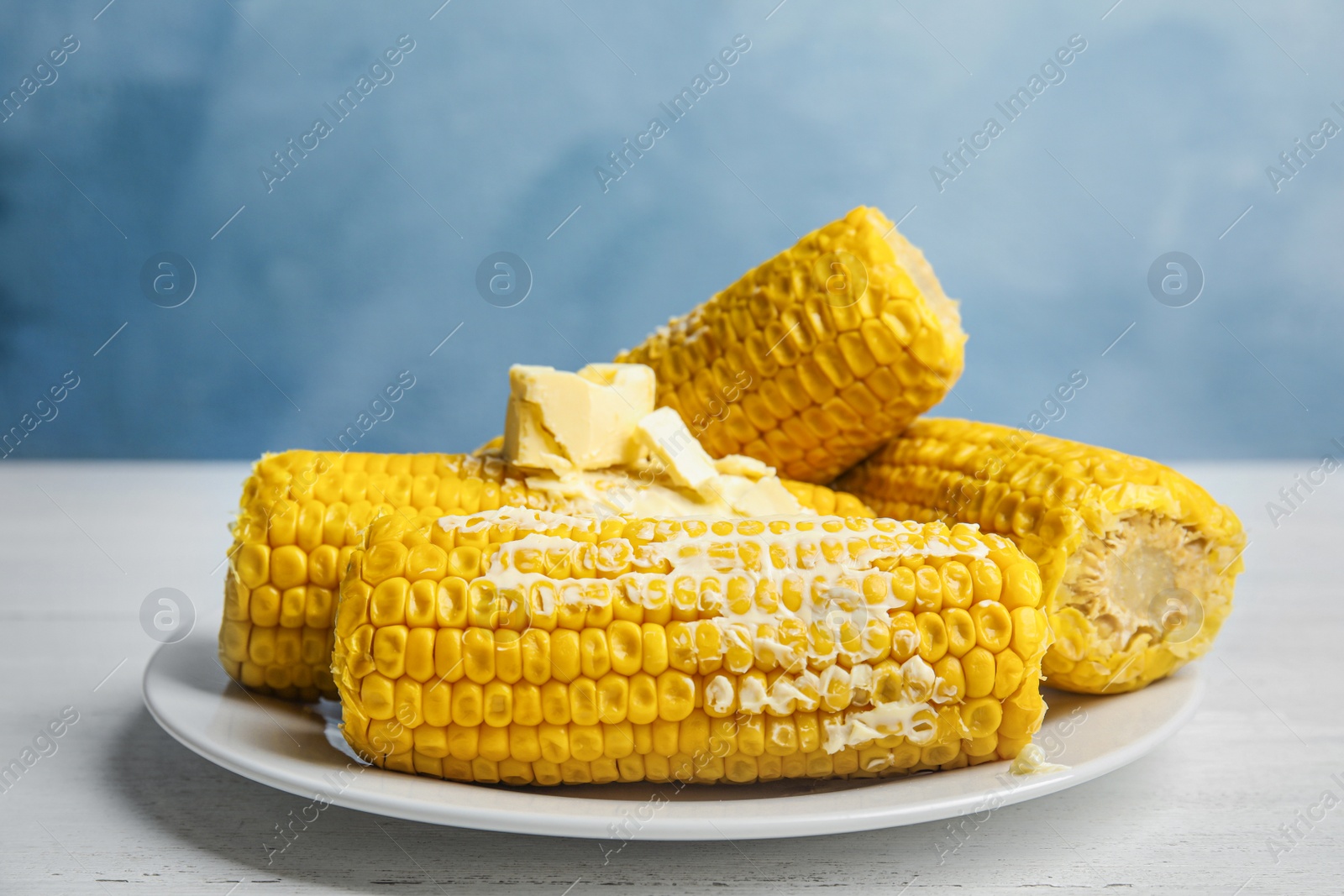 Photo of Delicious boiled corn with butter on white wooden table