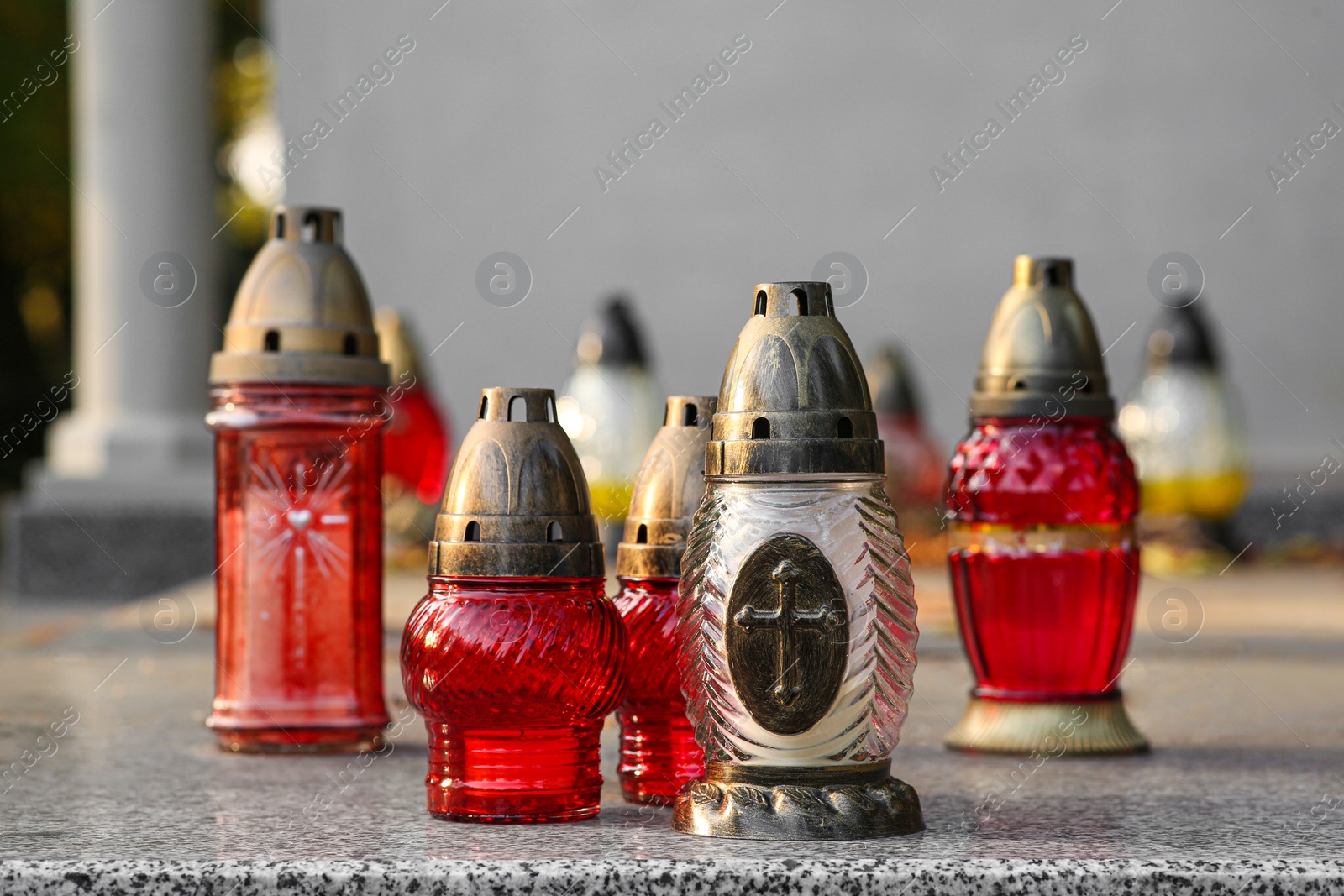 Photo of Different grave lanterns on granite tombstone outdoors. Funeral ceremony