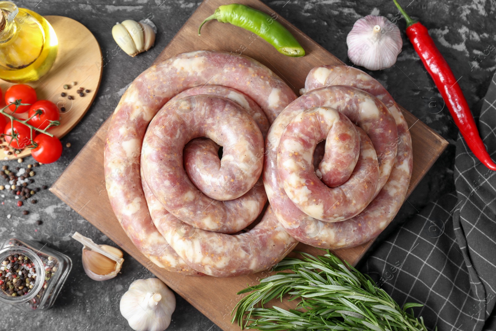 Photo of Raw homemade sausage, spices and other products on grey textured table, flat lay