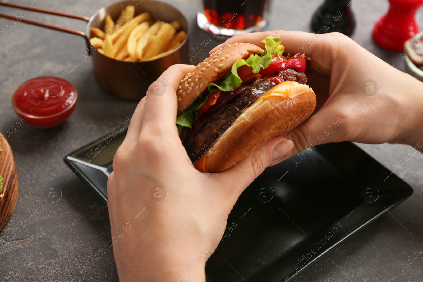 Photo of Woman holding tasty burger with bacon over grey table, closeup