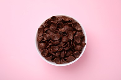 Photo of Breakfast cereal. Chocolate corn flakes in bowl on pink table, top view