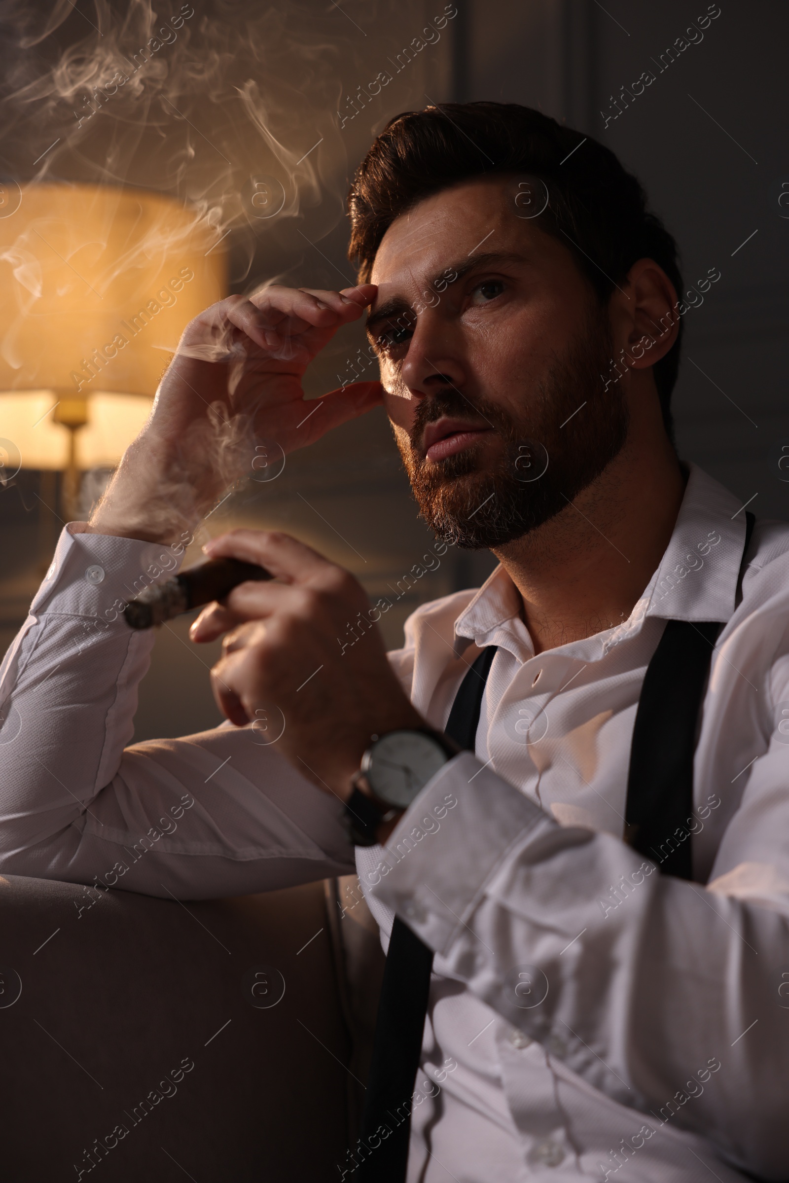 Photo of Handsome man smoking cigar at home in evening