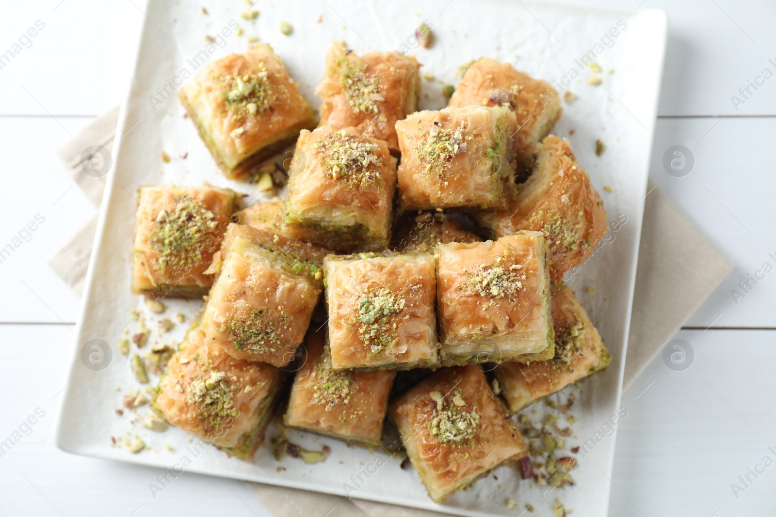 Photo of Delicious fresh baklava with chopped nuts on white wooden table, top view. Eastern sweets