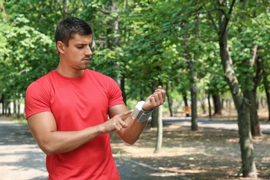 Young man checking pulse with medical device after training outdoors