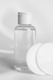 Bottle of micellar water and cotton pads on white background