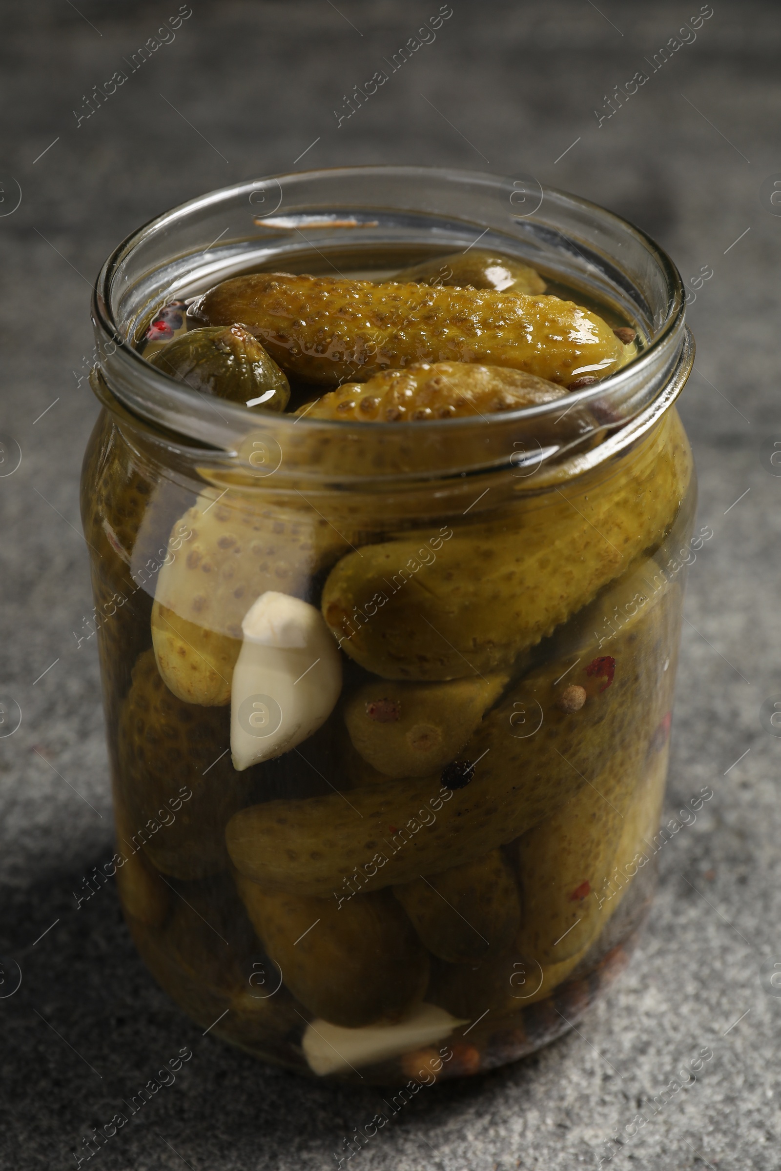 Photo of Tasty pickled cucumbers in glass jar on grey table, closeup