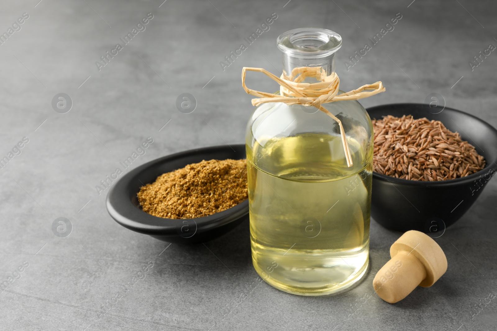 Photo of Caraway (Persian cumin) seeds, powder and essential oil on gray table, closeup