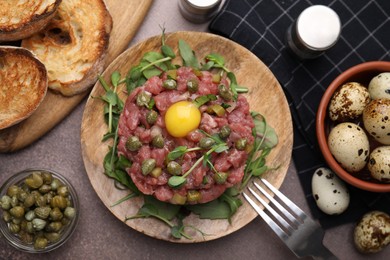 Photo of Tasty beef steak tartare served with yolk, capers and bread on brown table, flat lay