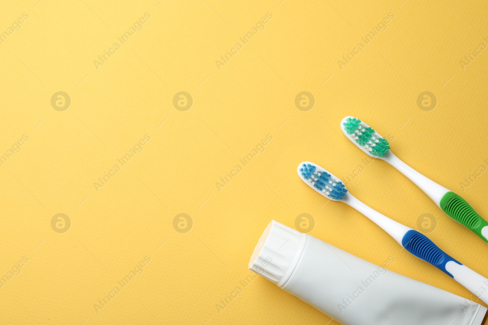 Photo of Blank tube of toothpaste and brushes on color background, top view with space for text