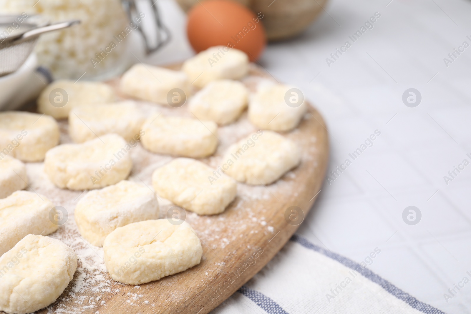 Photo of Making lazy dumplings. Wooden board with cut dough and flour on white tiled table, closeup. Space for text