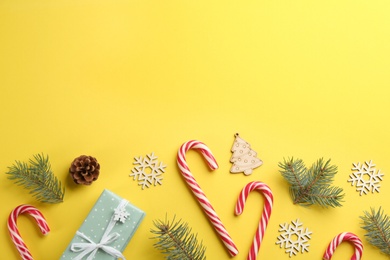 Flat lay composition with candy canes and Christmas decor on yellow background. Space for text