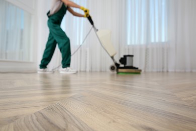 Photo of Blurred view of professional janitor cleaning parquet floor with polishing machine indoors, closeup