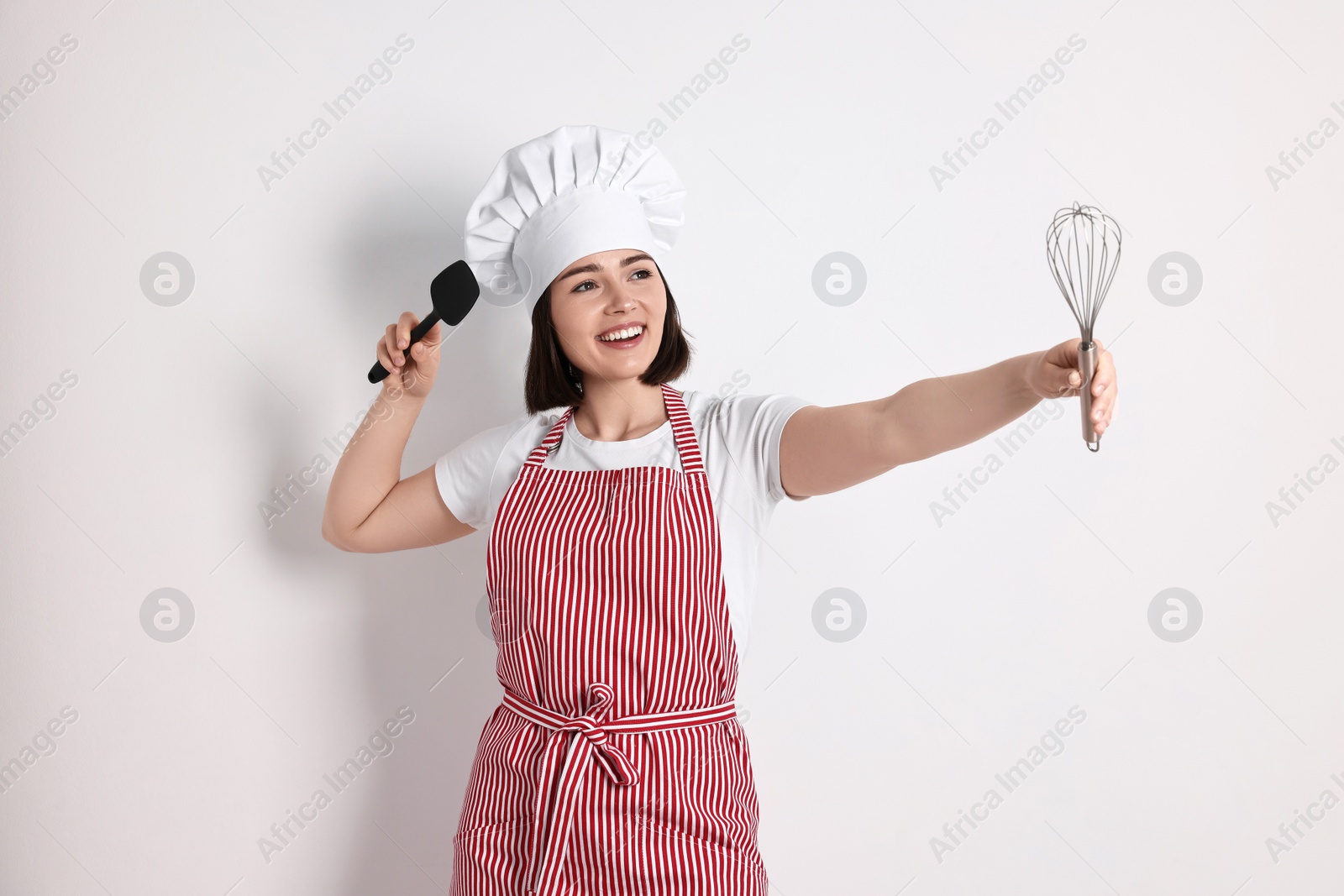 Photo of Happy confectioner with whisk and spatula on light grey background