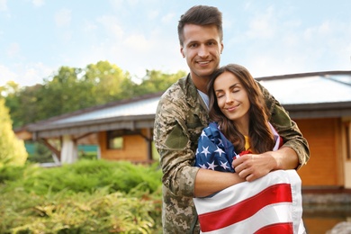 Man in military uniform with American flag and his wife outdoors