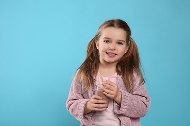 Photo of Cute little child with glass of tasty chocolate milk on light blue background, space for text