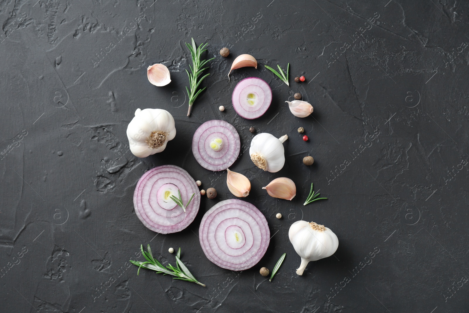 Photo of Fresh raw garlic, onion rings and spices on black table, flat lay