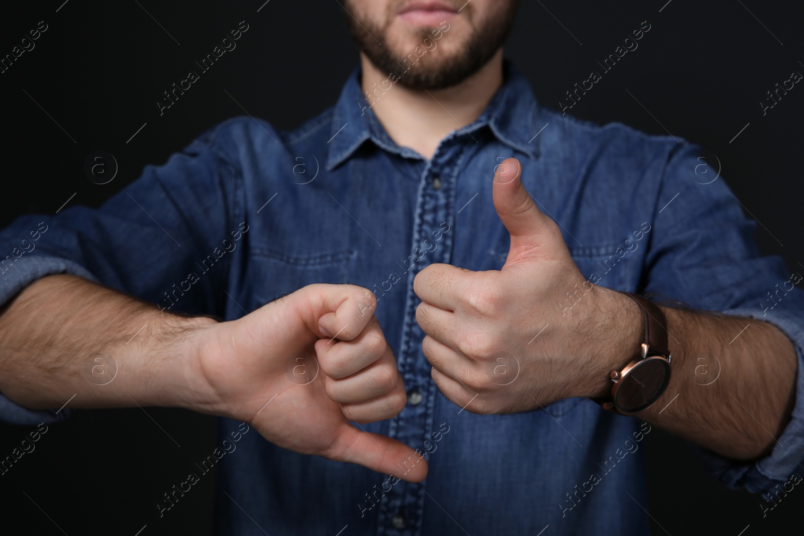 Photo of Man showing THUMB UP and DOWN gesture in sign language on black background, closeup