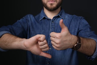Man showing THUMB UP and DOWN gesture in sign language on black background, closeup