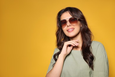 Happy beautiful woman with stylish sunglasses on orange background, space for text