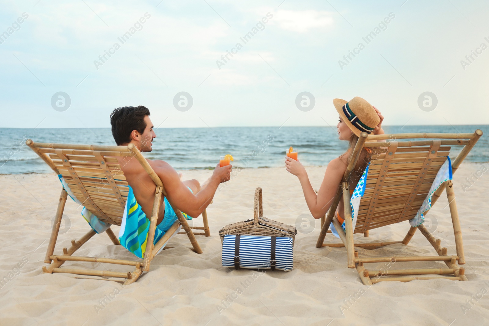 Photo of Happy young couple with cocktails sitting on deck chairs at sea beach