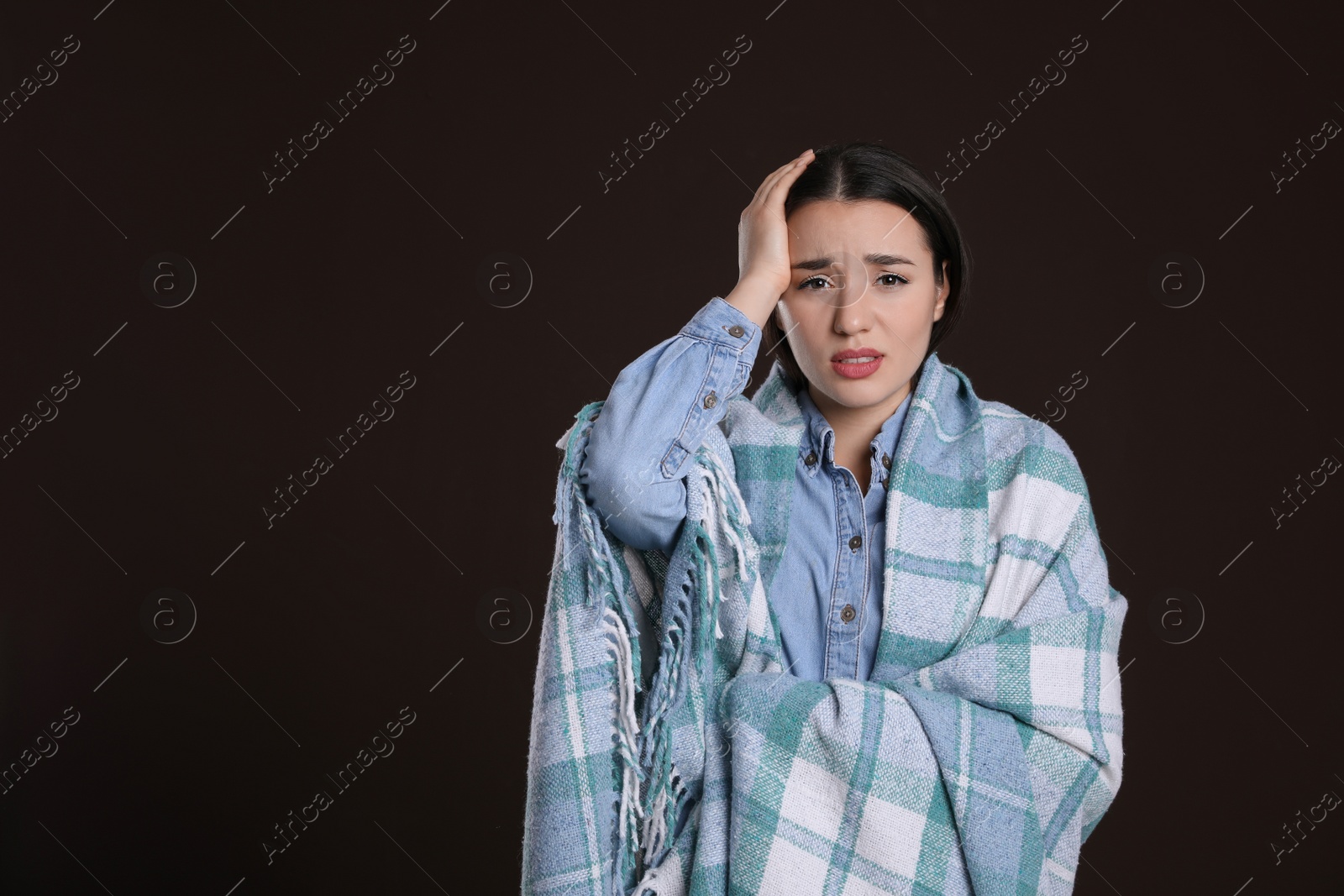 Photo of Young woman wrapped in blanket suffering from headache on dark background, space for text. Cold symptoms